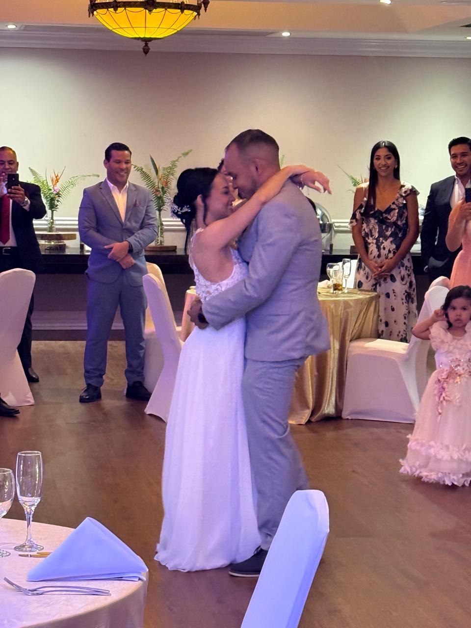 Novios abrazados durante su primer baile, rodeados de invitados en la recepción de su boda