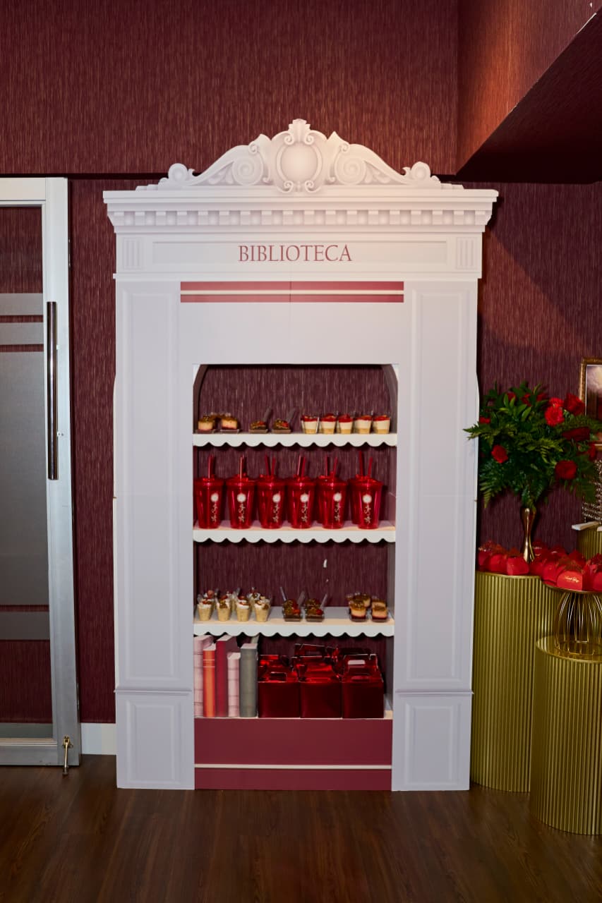 Mueble temático "Biblioteca" decorado con postres, vasos personalizados y cajas rojas para la Experiencia Creativa Basic