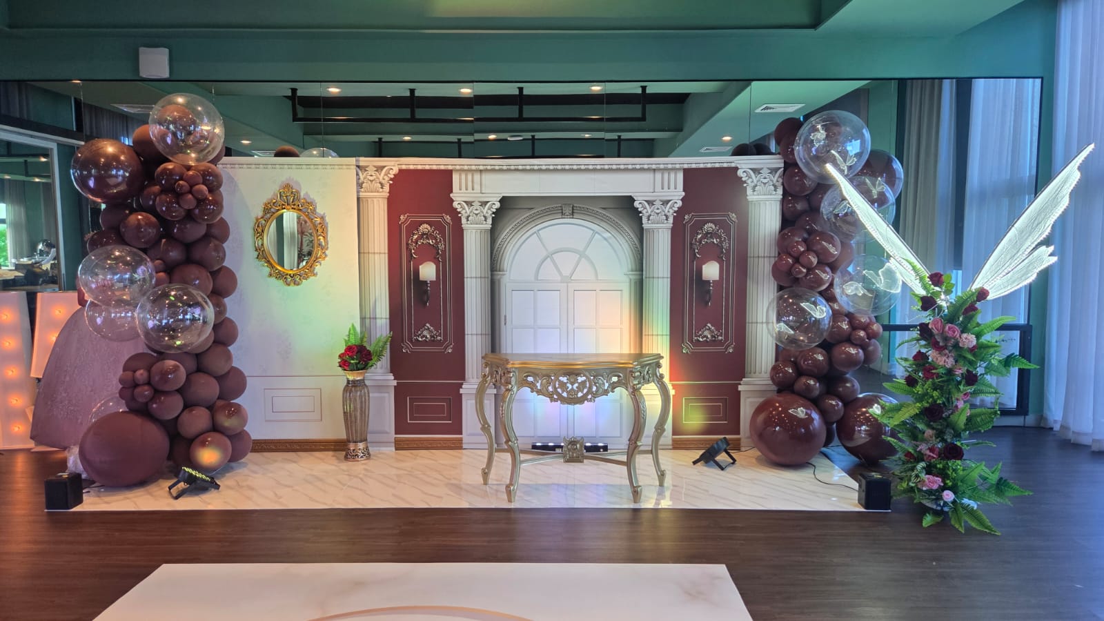 Escenario completo temático con arcos de globos, espejo decorativo, consola dorada y arreglo floral con alas de hada para la Experiencia Creativa Basic